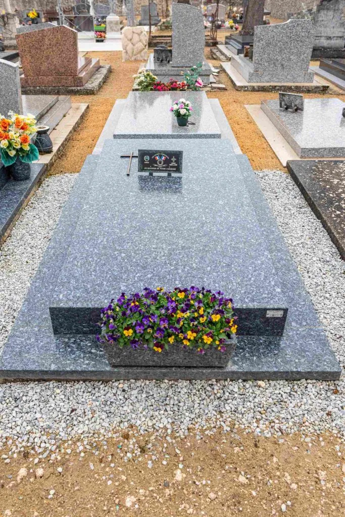 Tombe en granite gris fleurie de pensées violets et jaunes dans un cimetière.