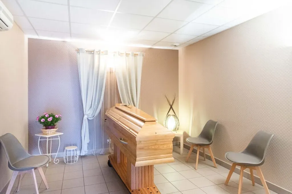 Salon funéraire intime et chaleureux accueillant un cercueil en bois clair.