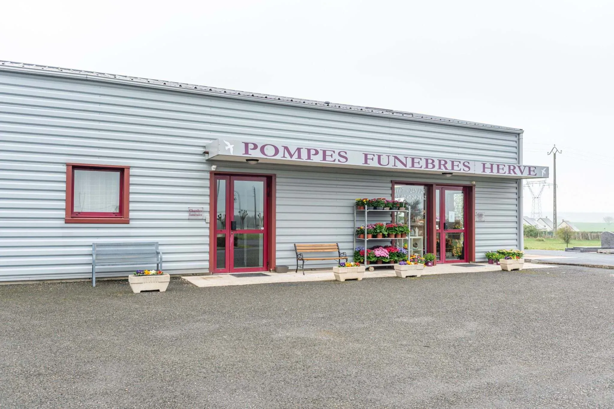 Façade des Pompes Funèbres Hervé avec portes vitrées, bancs et fleurs en devanture.