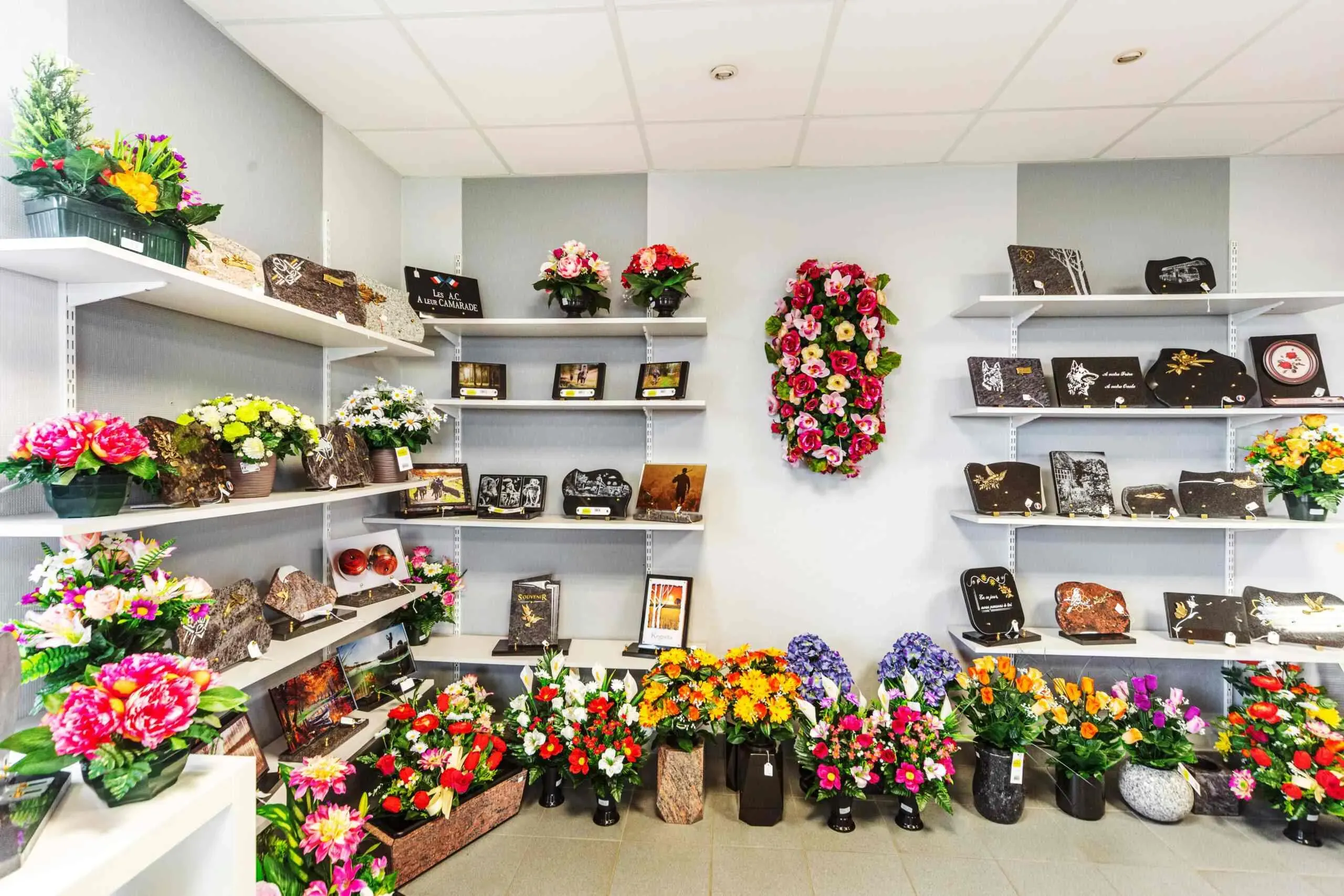 Rayonnages de magasin présentant un vaste choix de plaques funéraires et de fleurs artificielles.